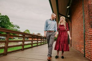 Couple walking hand in hand along a wooden bridge near a brick barn in countryside.