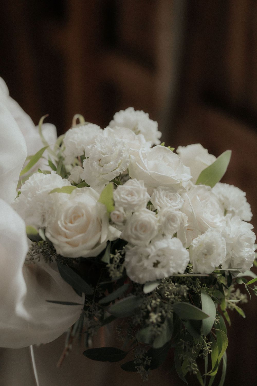 An elegant white wedding bouquet with roses and eucalyptus leaves arranged in soft natural light.