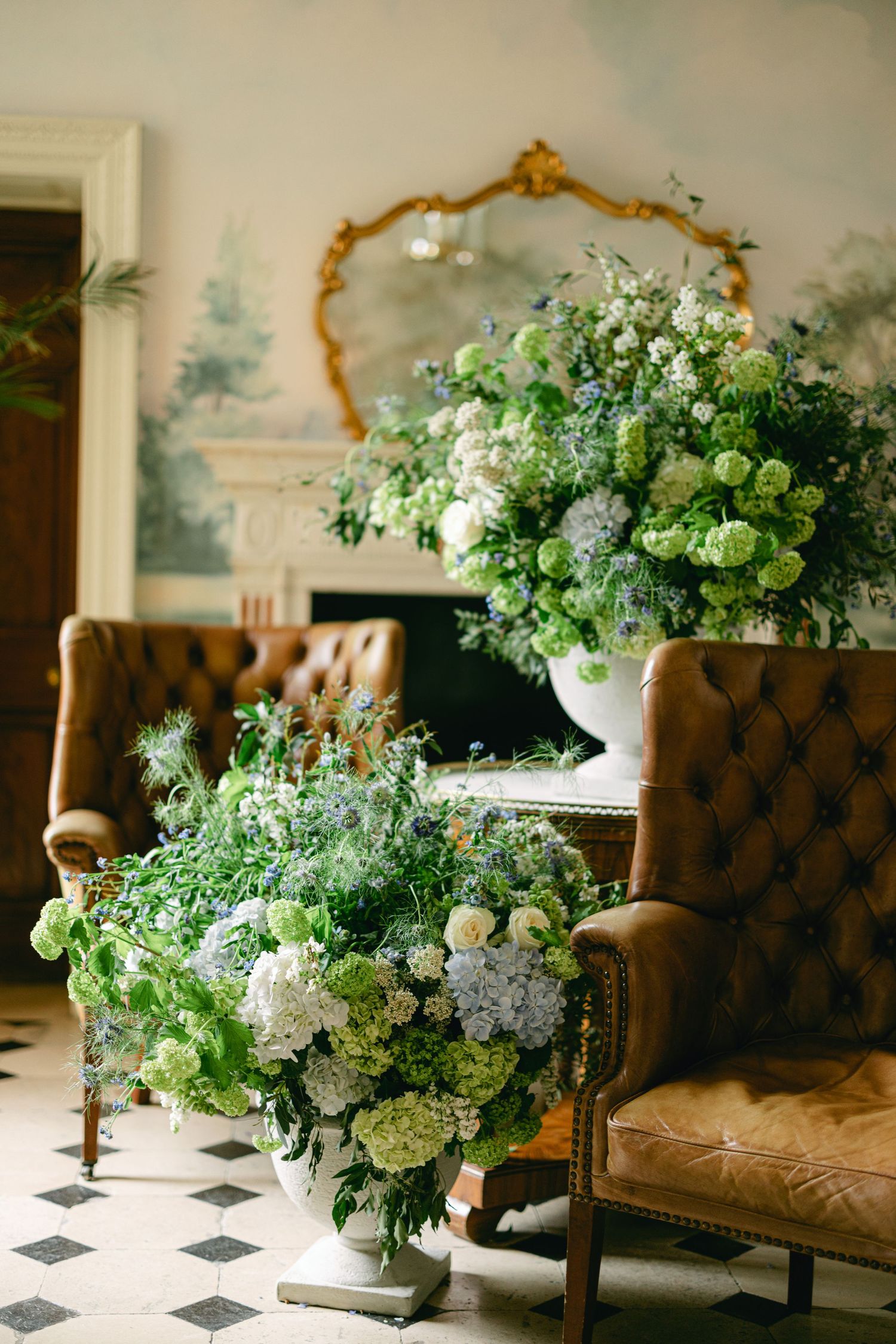 Luxurious floral arrangements with green and white blooms displayed in an ornate room with vintage furniture.