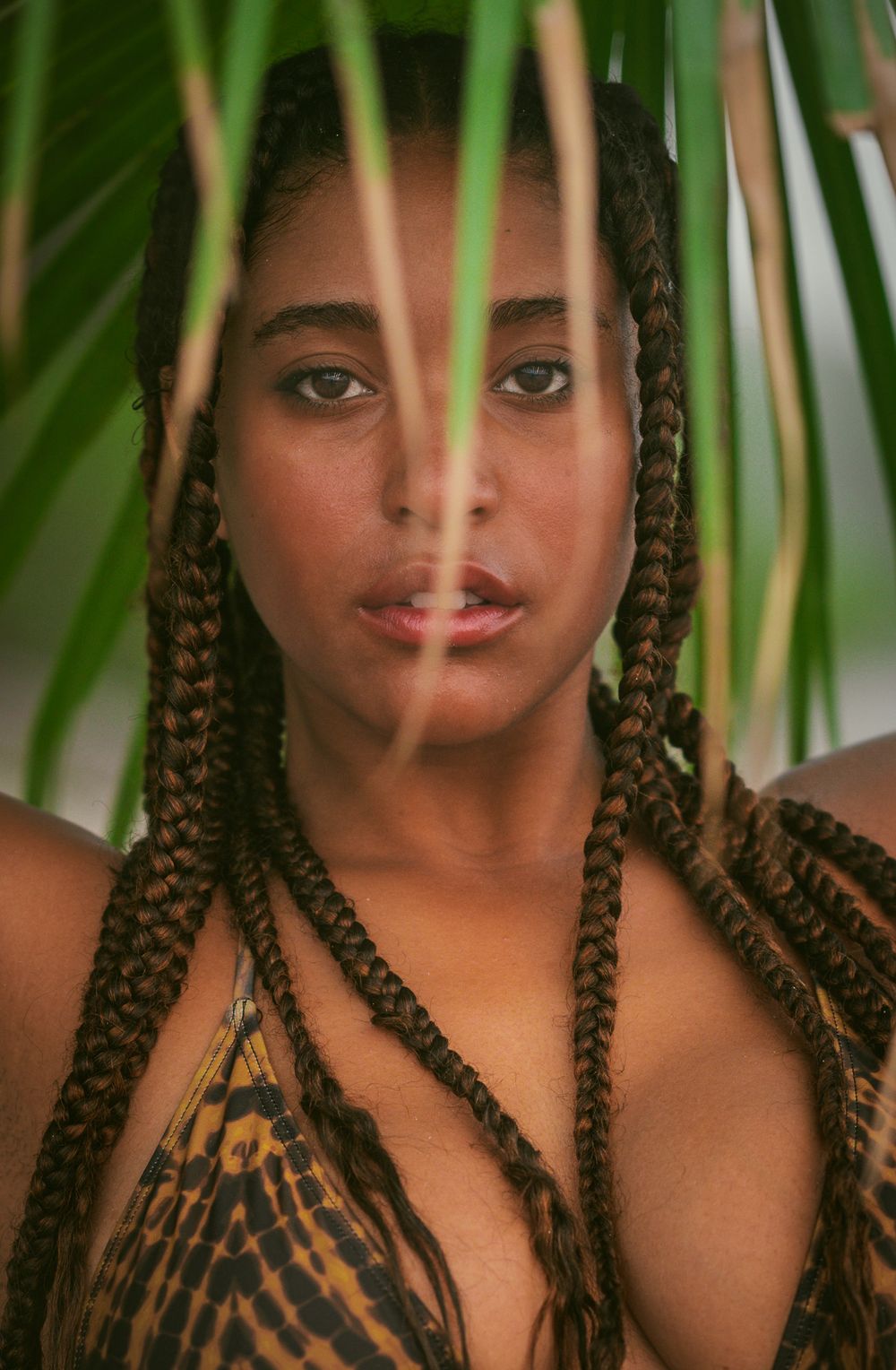 Creative portrait through palm leaves showing braided hairstyle.