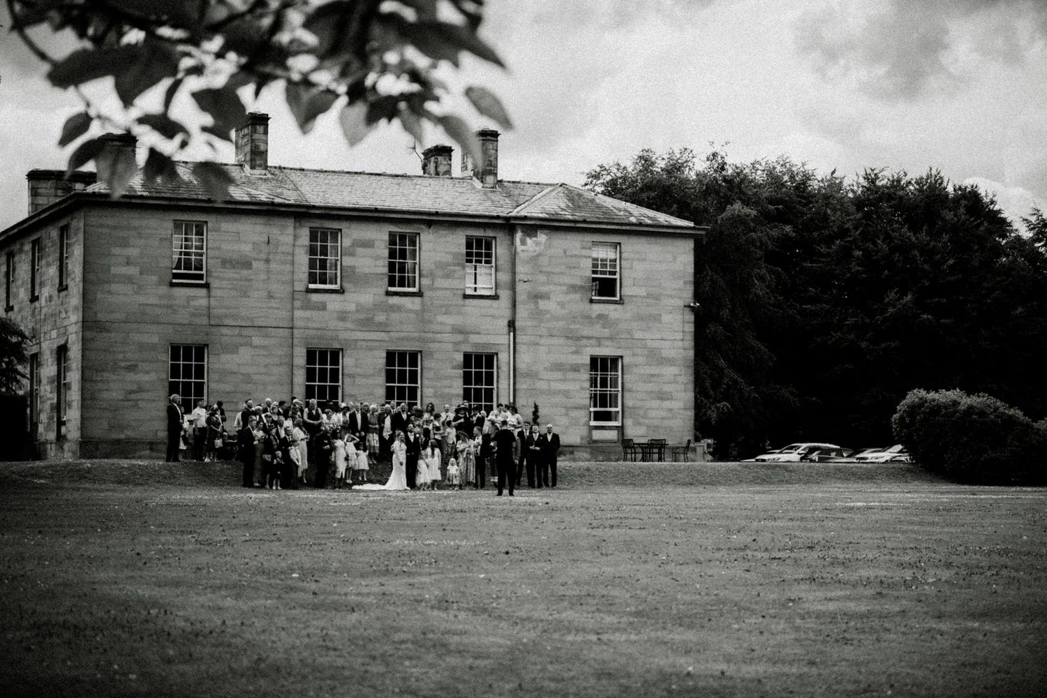 Wedding party gathered outside a grand historic mansion in black and white. Saltmarshe Hall