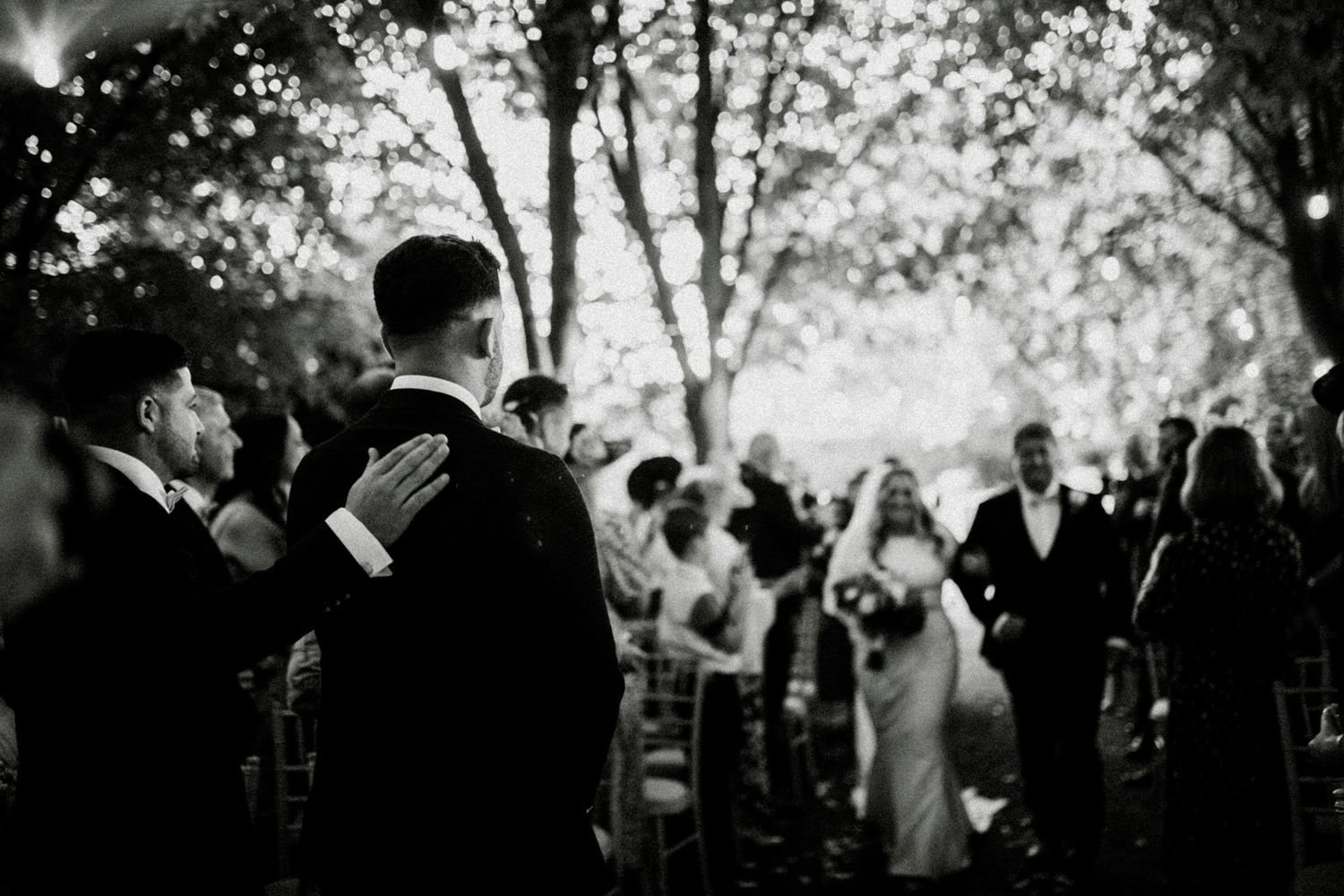 Silhouetted wedding party celebrates outdoors under trees at dusk. Saltmarshe Hall