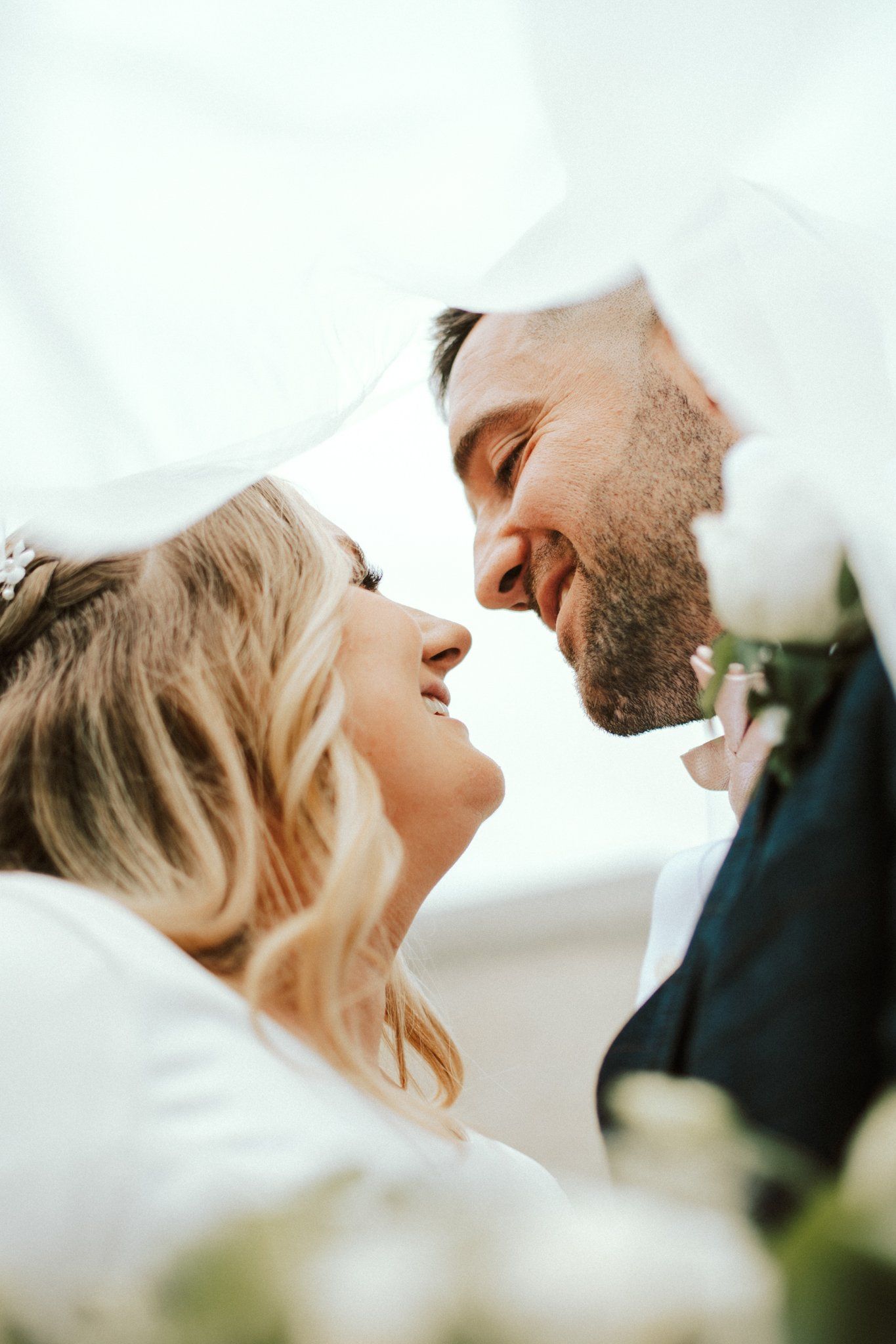 Intimate moment between newlyweds sharing a romantic gesture against bright background.