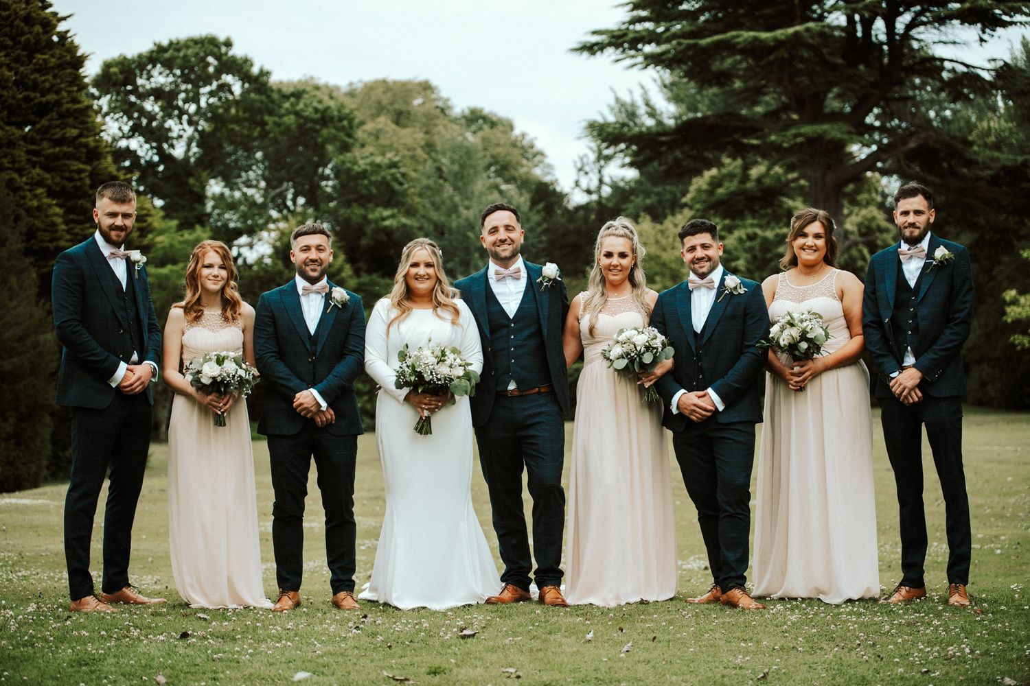 Wedding party in navy suits and blush dresses pose together on elegant grounds. Saltmarshe Hall