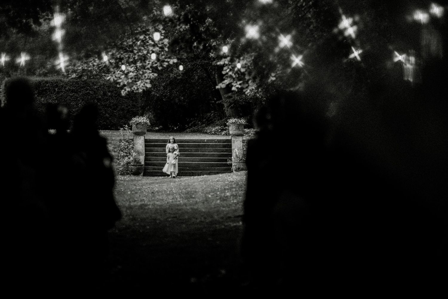 Twinkling lights strung across a rustic wooden arbor create a romantic outdoor wedding setting at dusk. Saltmarshe Hall