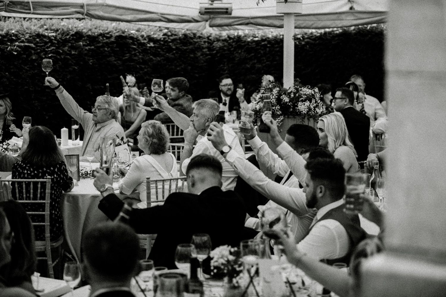 Wedding reception guests raise their glasses in celebration during an outdoor party. Saltmarshe Hall