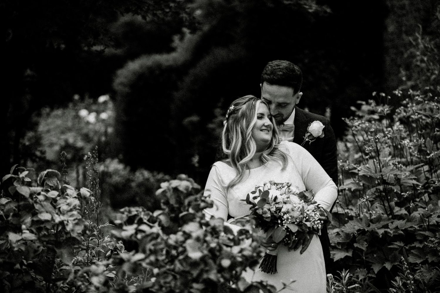 A romantic black and white wedding portrait captured in a lush garden setting with a beautiful bouquet. Saltmarshe Hall