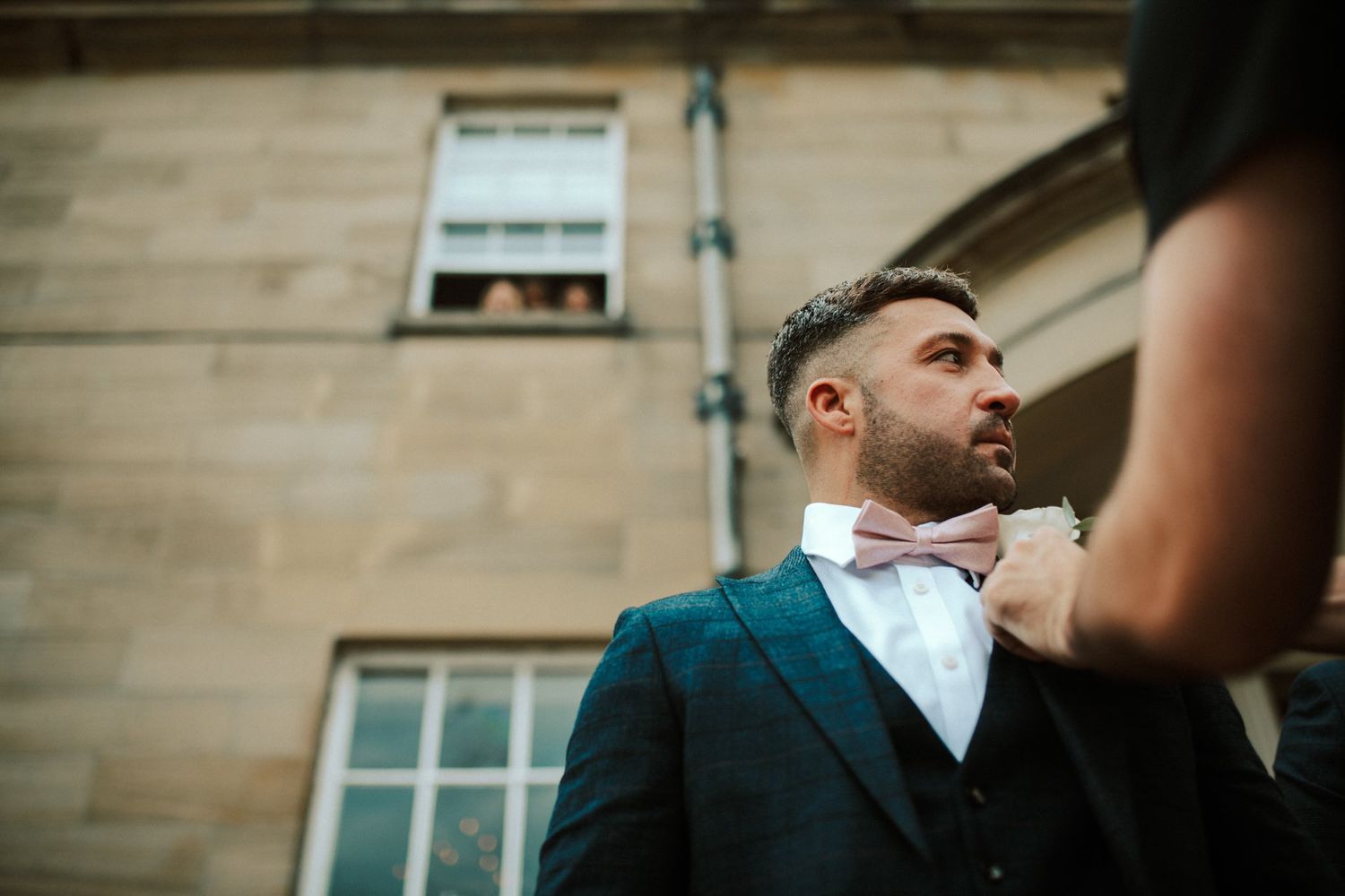 Someone adjusts a pink bow tie on a formal blue suit jacket. Saltmarshe Hall