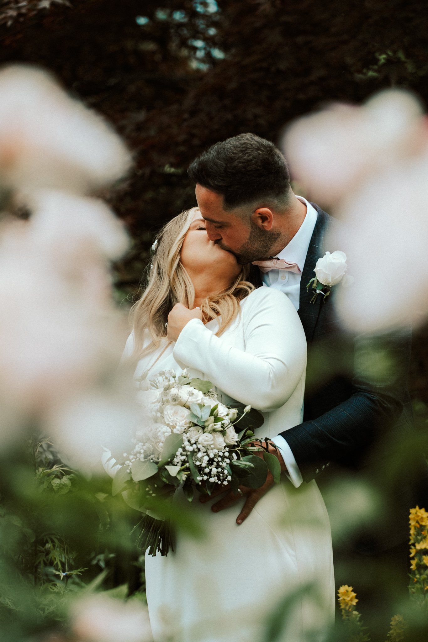 Romantic portrait of newlyweds embracing outdoors with soft florals in the foreground. Saltmarshe Hall