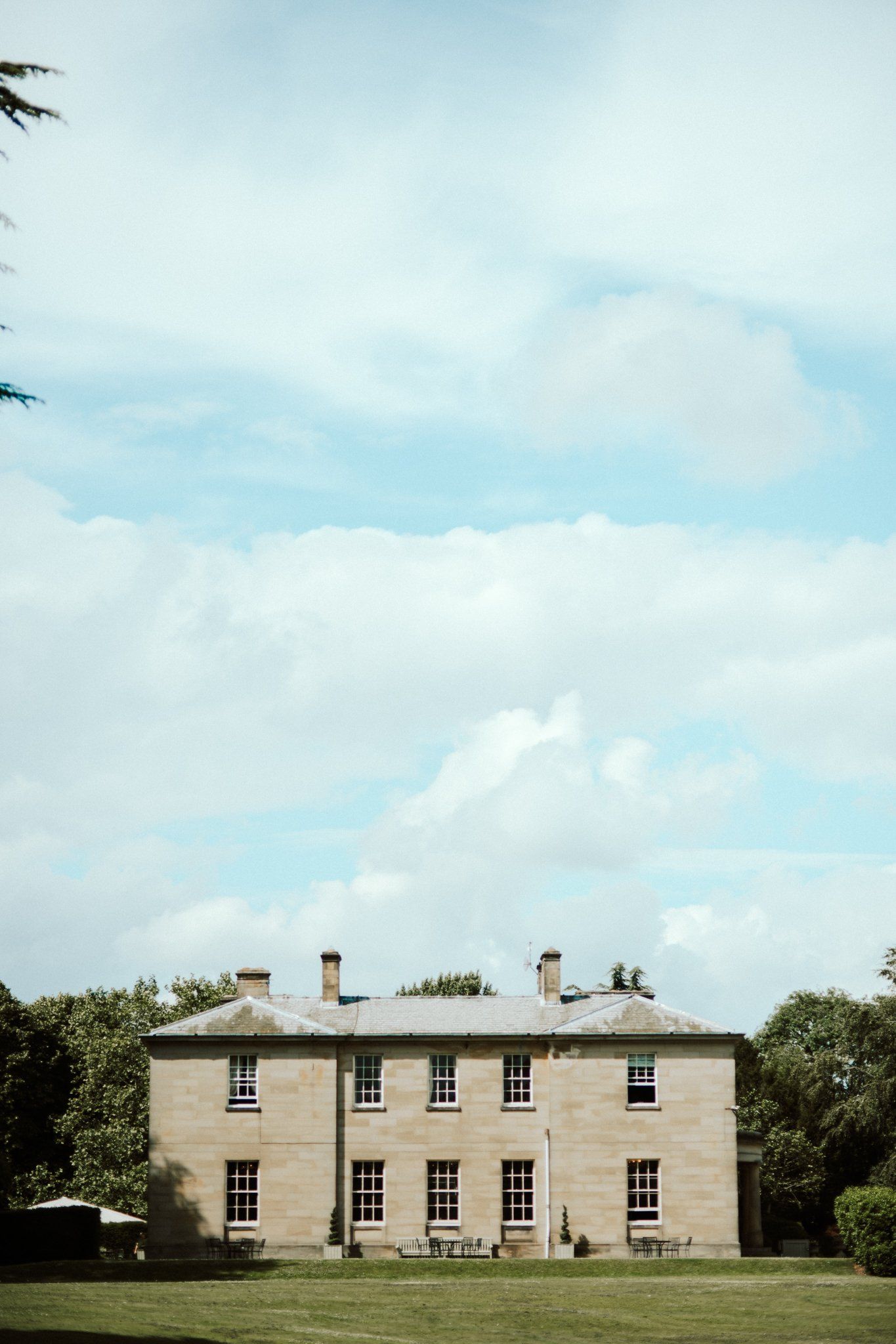 Large stone mansion with symmetrical windows on a sunny day with cloudy blue sky. Saltmarshe Hall