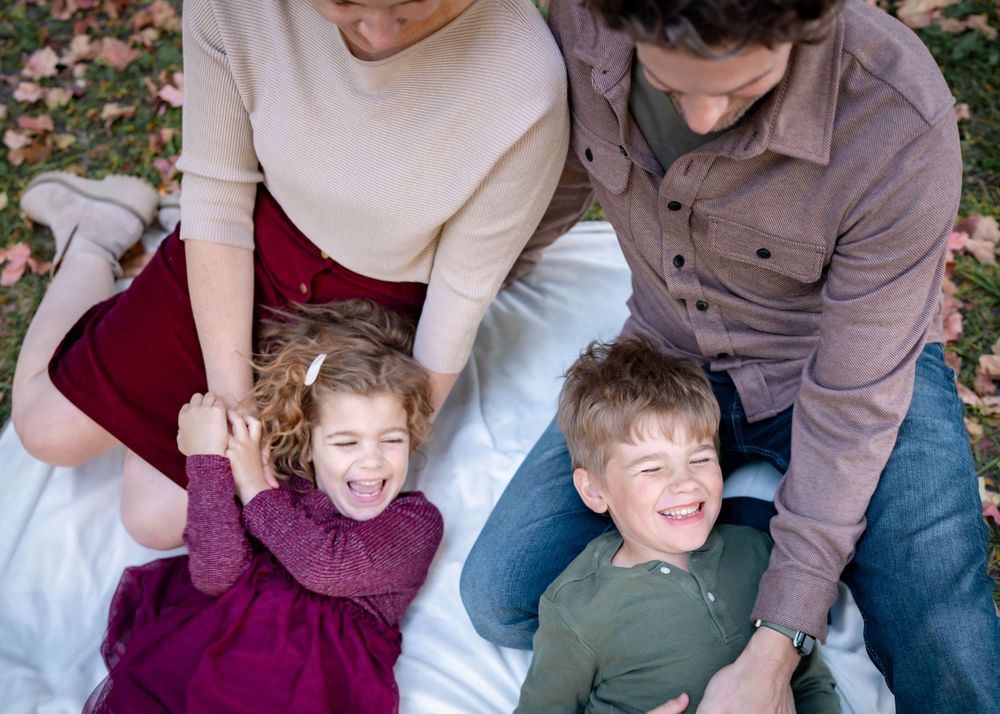 Overhead view of a family of four laughing together on a white blanket surrounded by fall foliage.