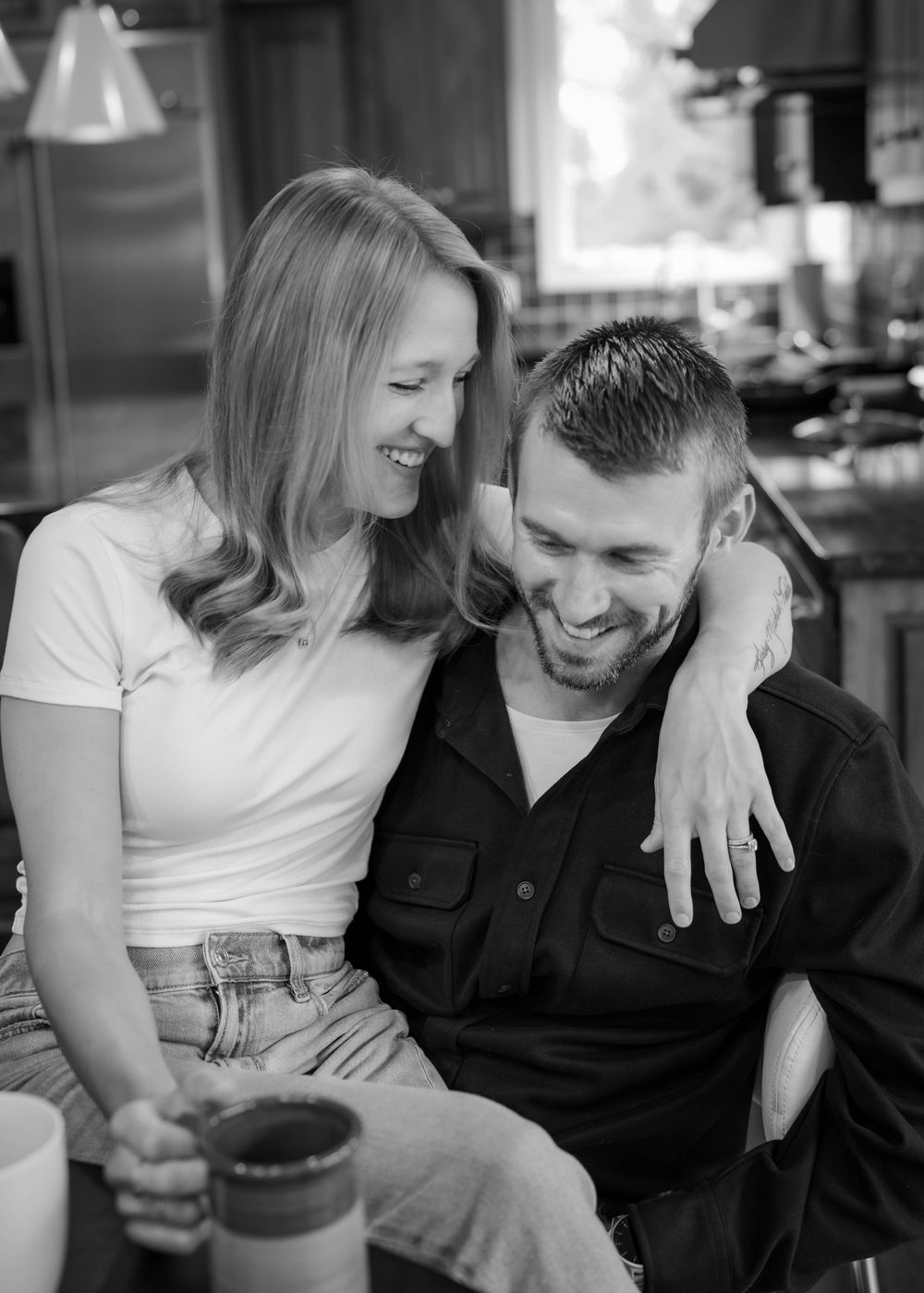 Happy smiling couple sharing a laugh together indoors in black and white lifestyle portrait photo.
