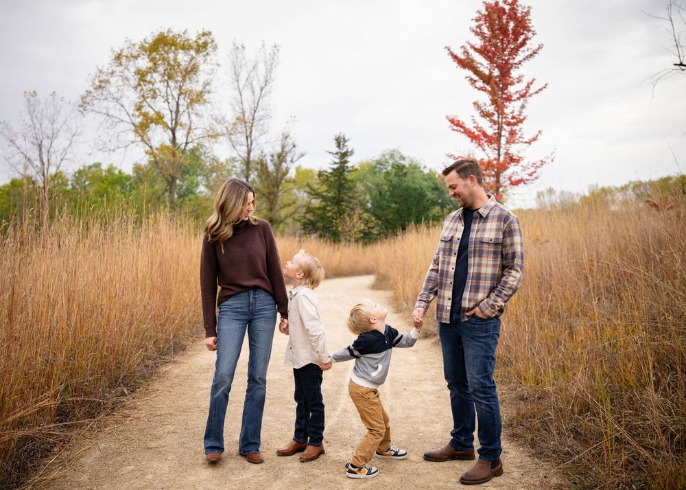 A family of three walks along a scenic autumn path with colorful fall foliage in the background.