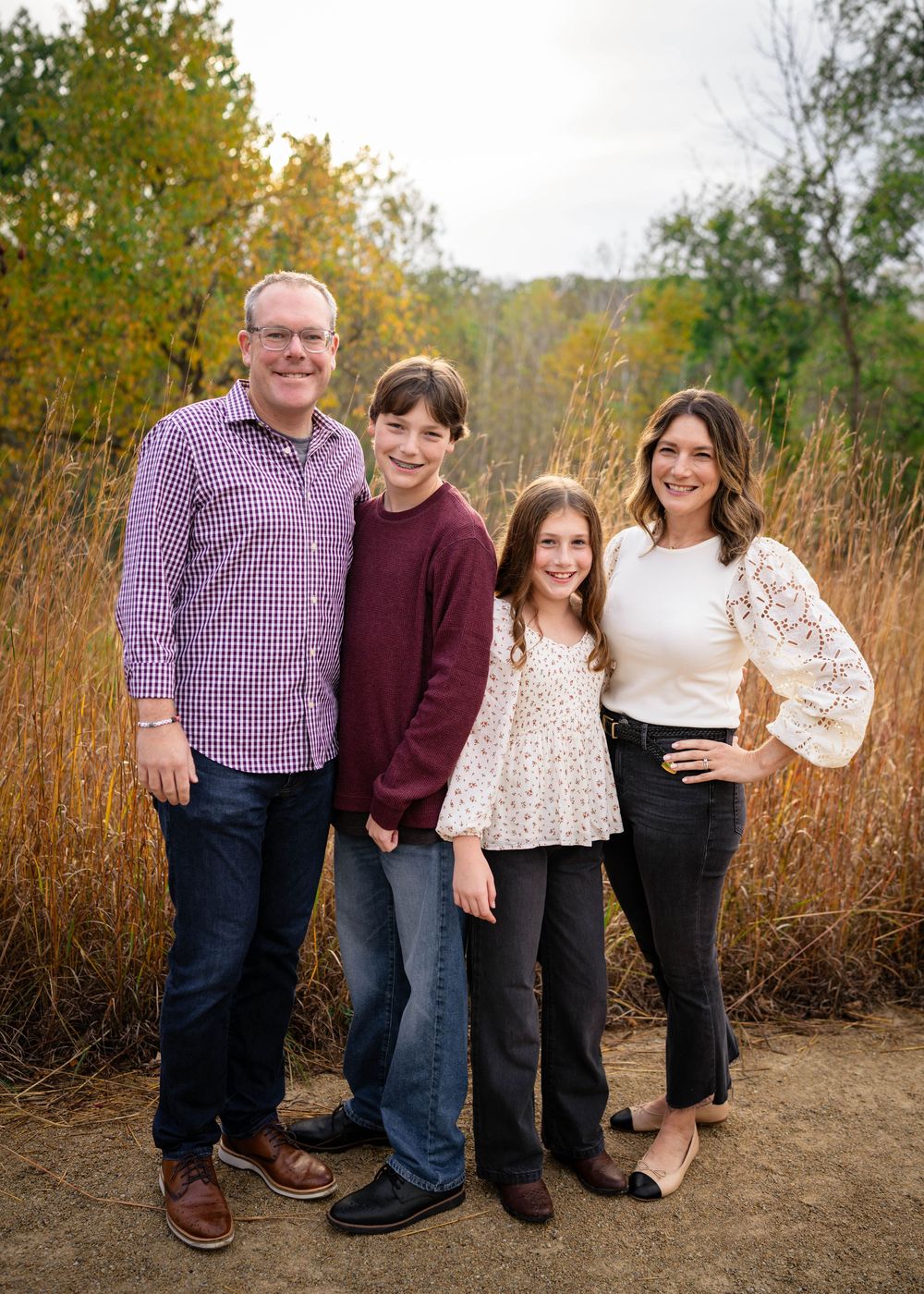 A family of four smiles together in front of colorful autumn foliage during an outdoor photo session.