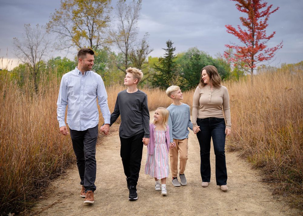 A family of five walks hand in hand along a dirt path surrounded by vibrant fall foliage.