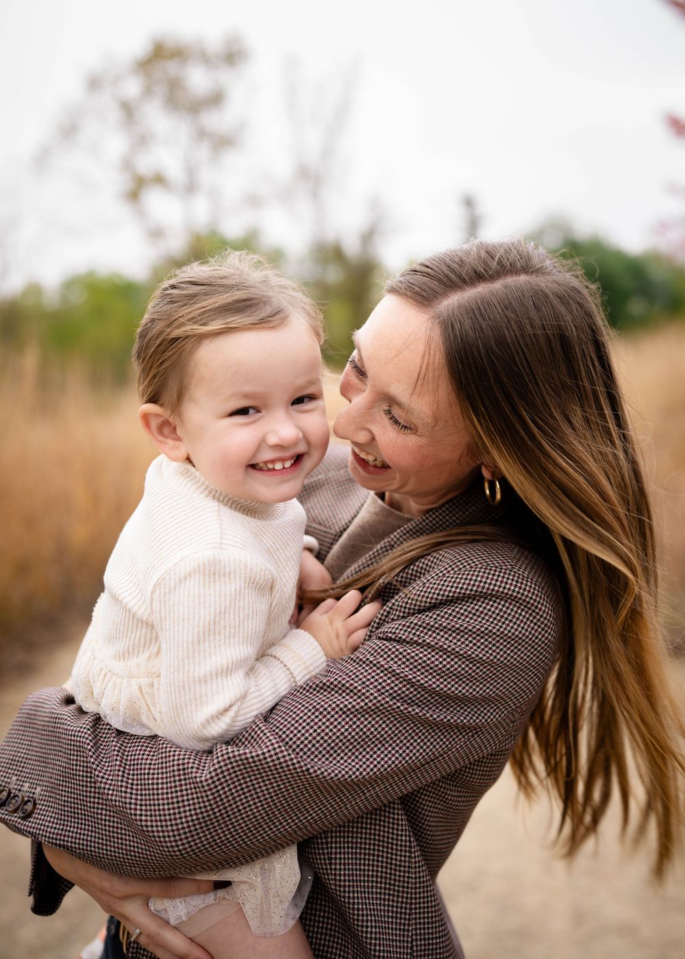 A brunette mother holds her smiling toddler daughter close during an outdoor fall portrait session.