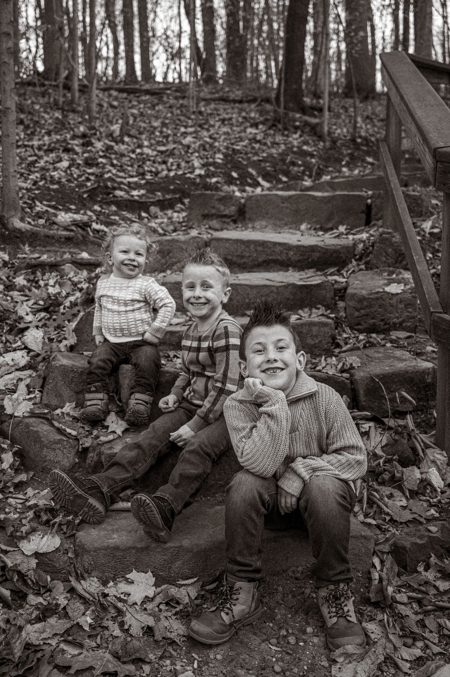 A black and white portrait of three smiling brothers sitting on stone steps in autumn woods.