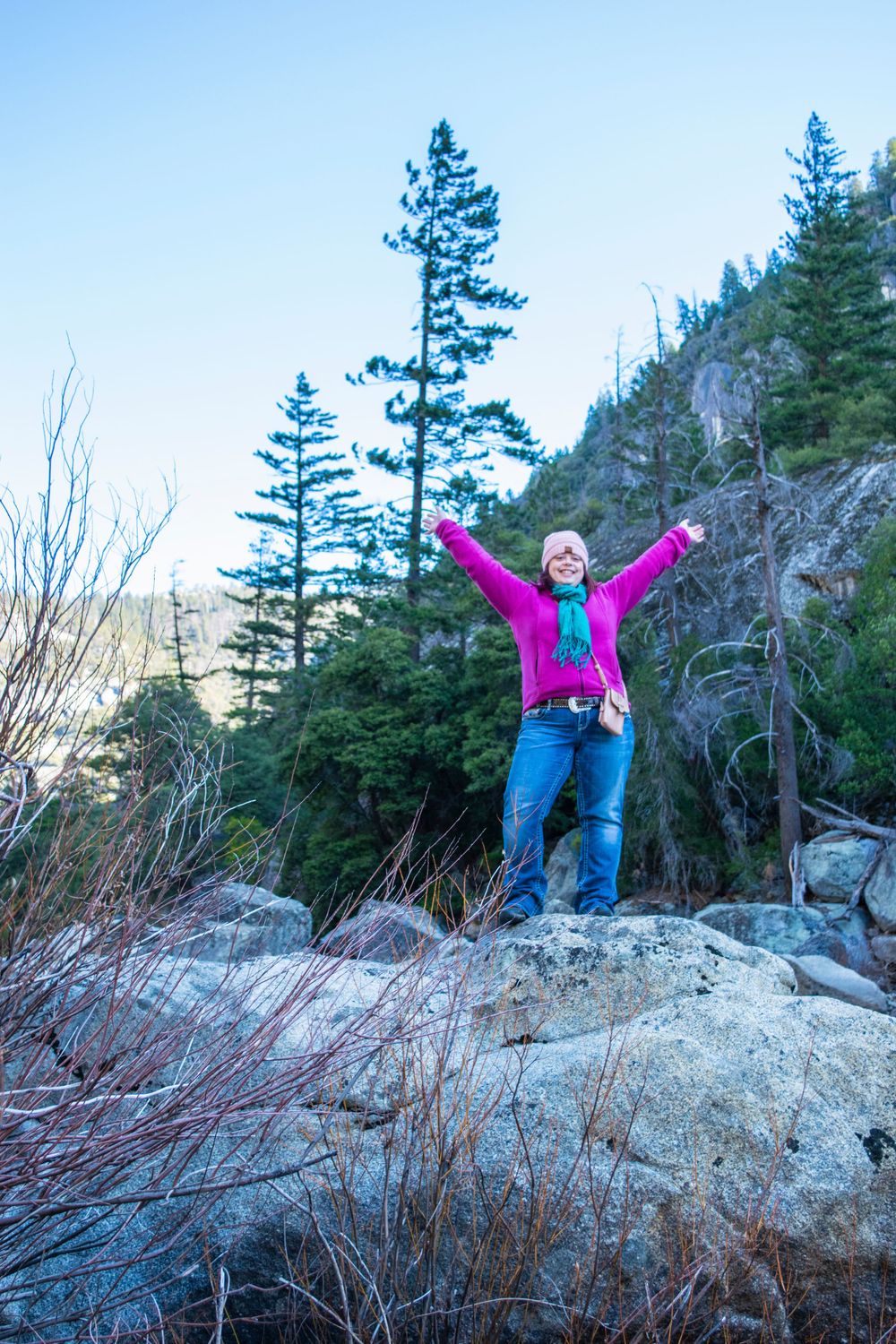 Joyful outdoor enthusiast celebrates on rocky outcrop with mountain scenery behind.