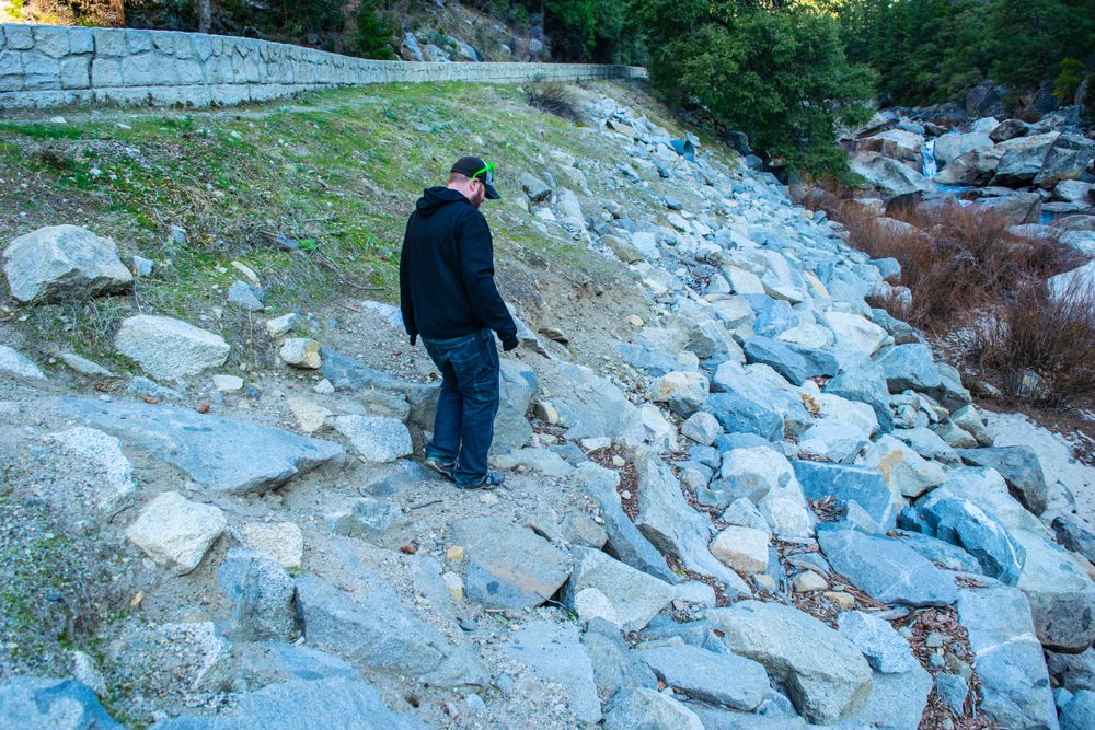 Hiker navigates rocky terrain along mountain trail beside river.