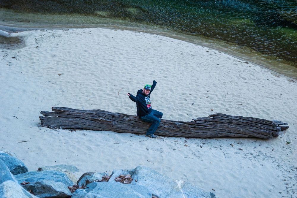 Adventure seeker sits on large fallen log in snowy riverbank.
