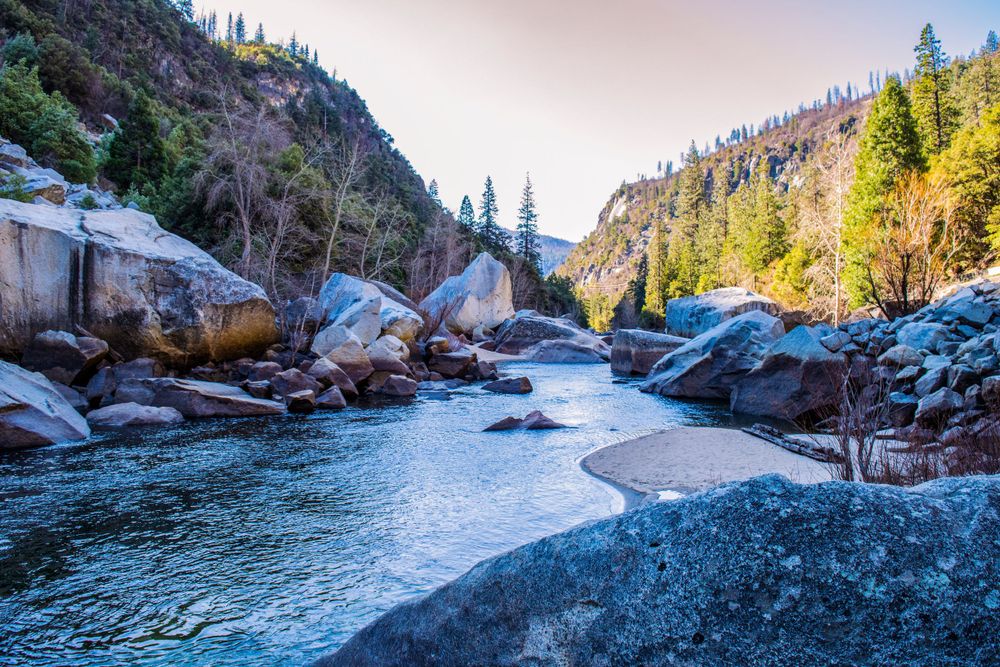 Frozen river meanders through rocky mountain canyon with evergreen forest.
