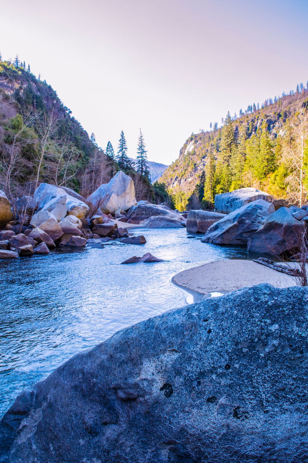Icy mountain river winds through granite boulder field in winter landscape.