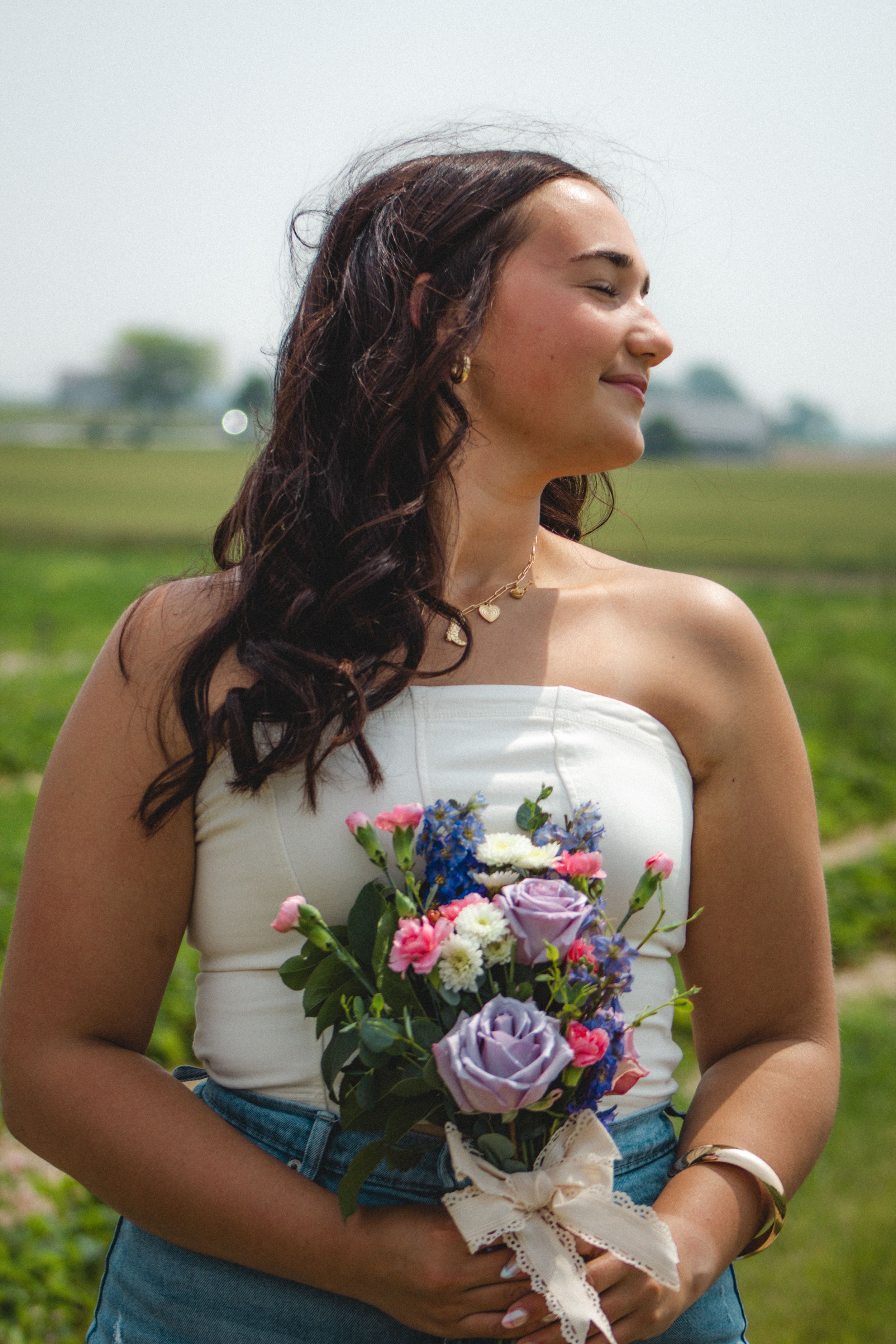 a girl feeling the sun with a bouquet of pink and purple flowers