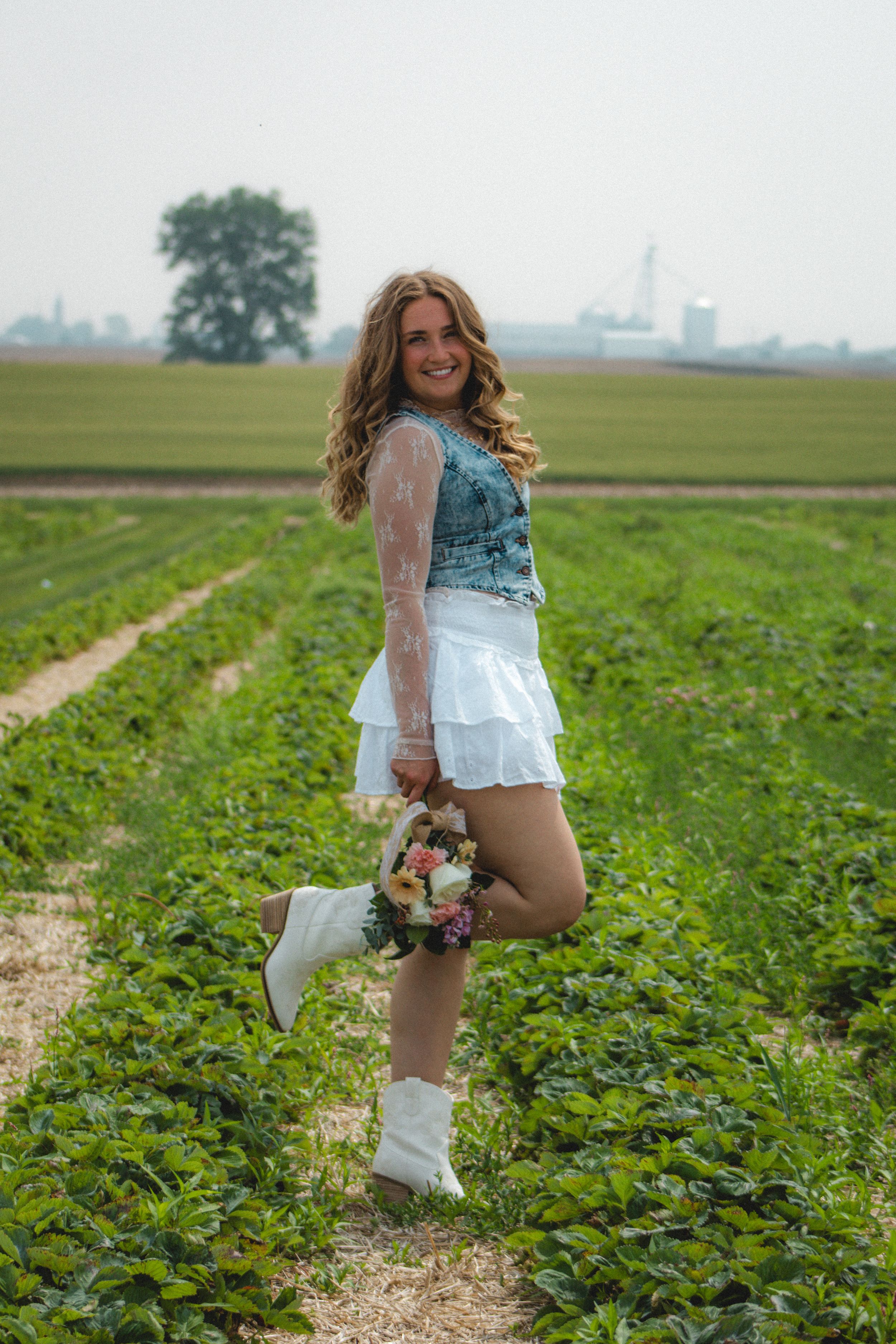 a girl posing with one leg up and with a bouquet of pink and purple flowers