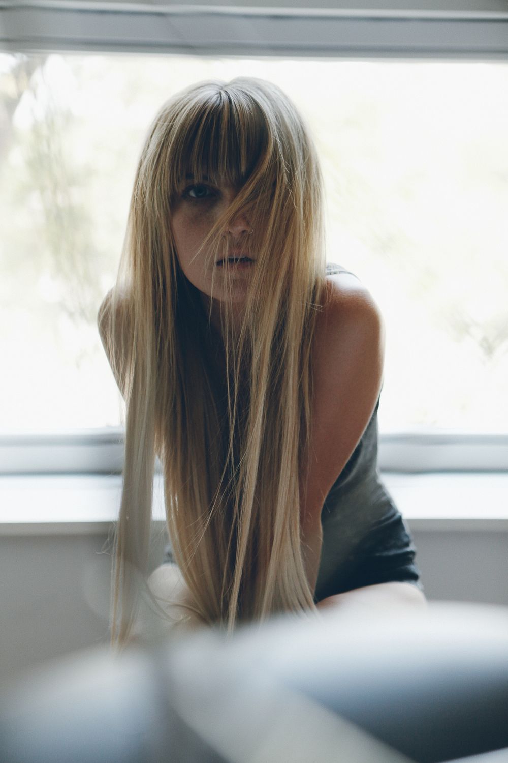 Artistic portrait with long blonde hair and bangs in soft natural window light.
