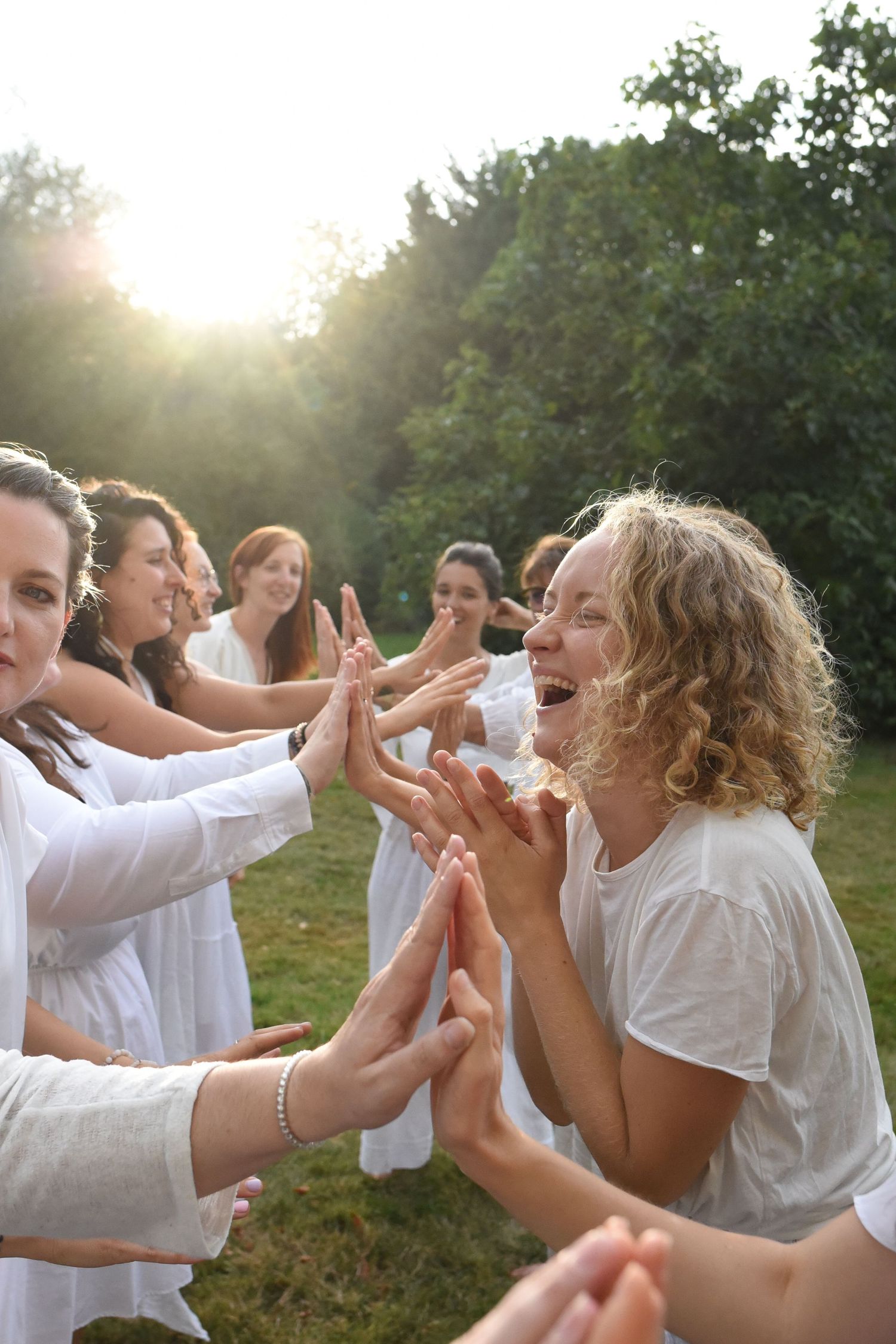 Group of people in white clothing playing joyfully outdoors in golden sunlight.