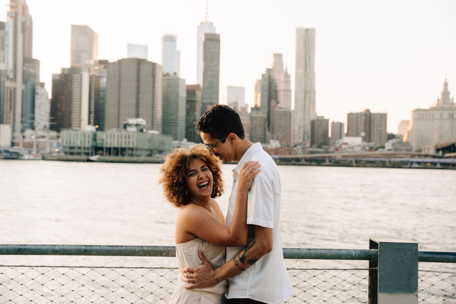 A couple embracing in autumn by a lake with NYC skyscrapers in the background.