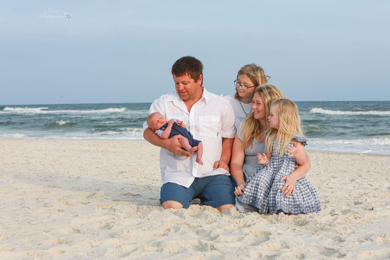Family sitting together on beach sand with ocean waves in background.