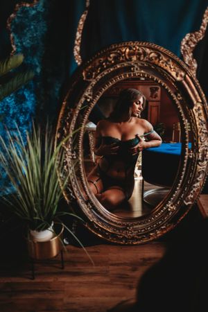 An ornate gold vintage mirror reflects candlelight in a moody interior setting with a potted plant nearby.