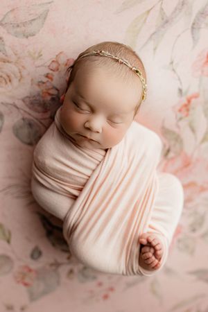 Sleeping newborn baby girl swaddled in pink wrap wearing floral headband on pink floral backdrop. Portsmouth Ohio Greenup Kentucky Grayson
