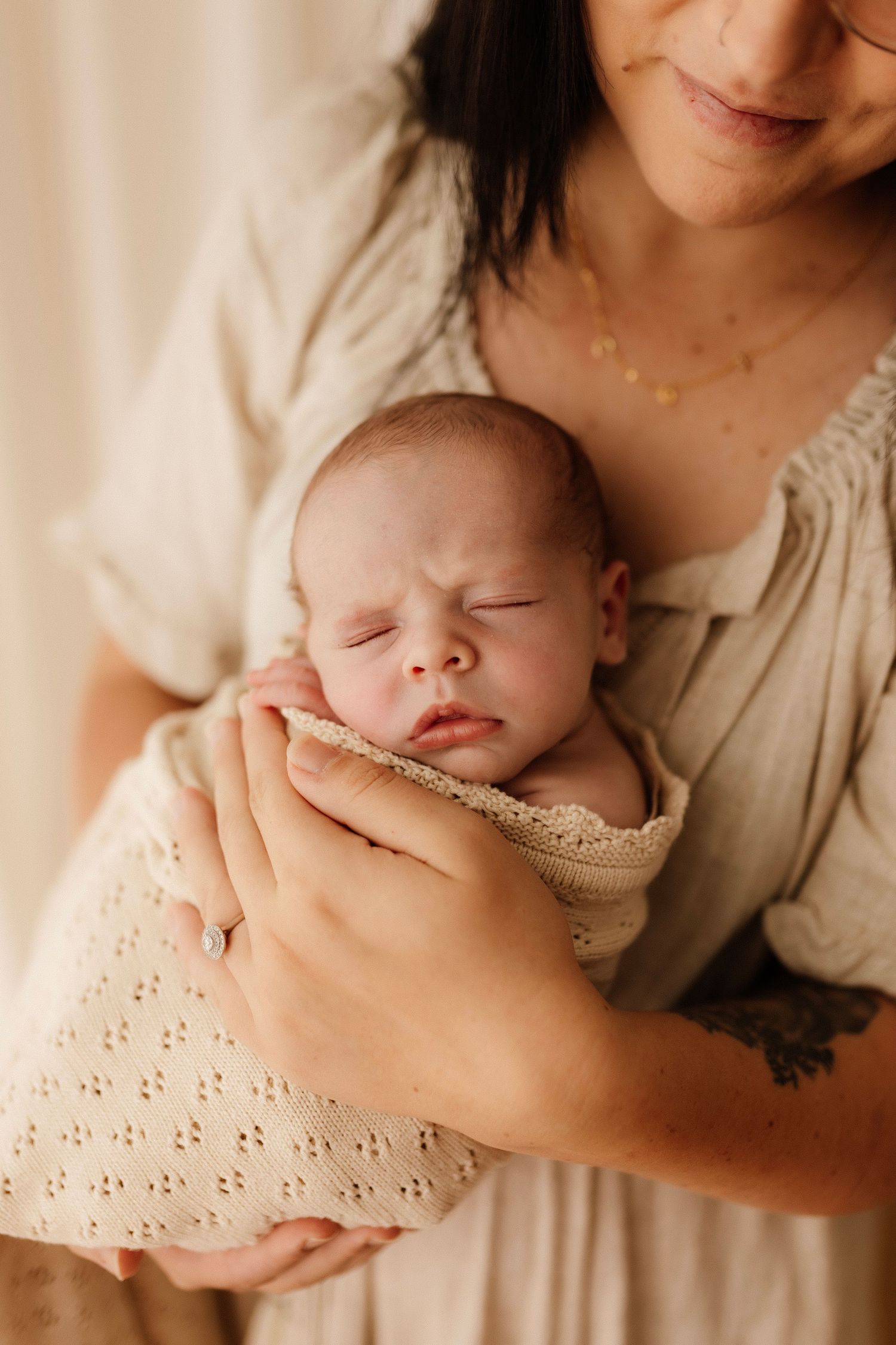 Sleeping newborn cradled gently in soft beige fabrics in natural light.