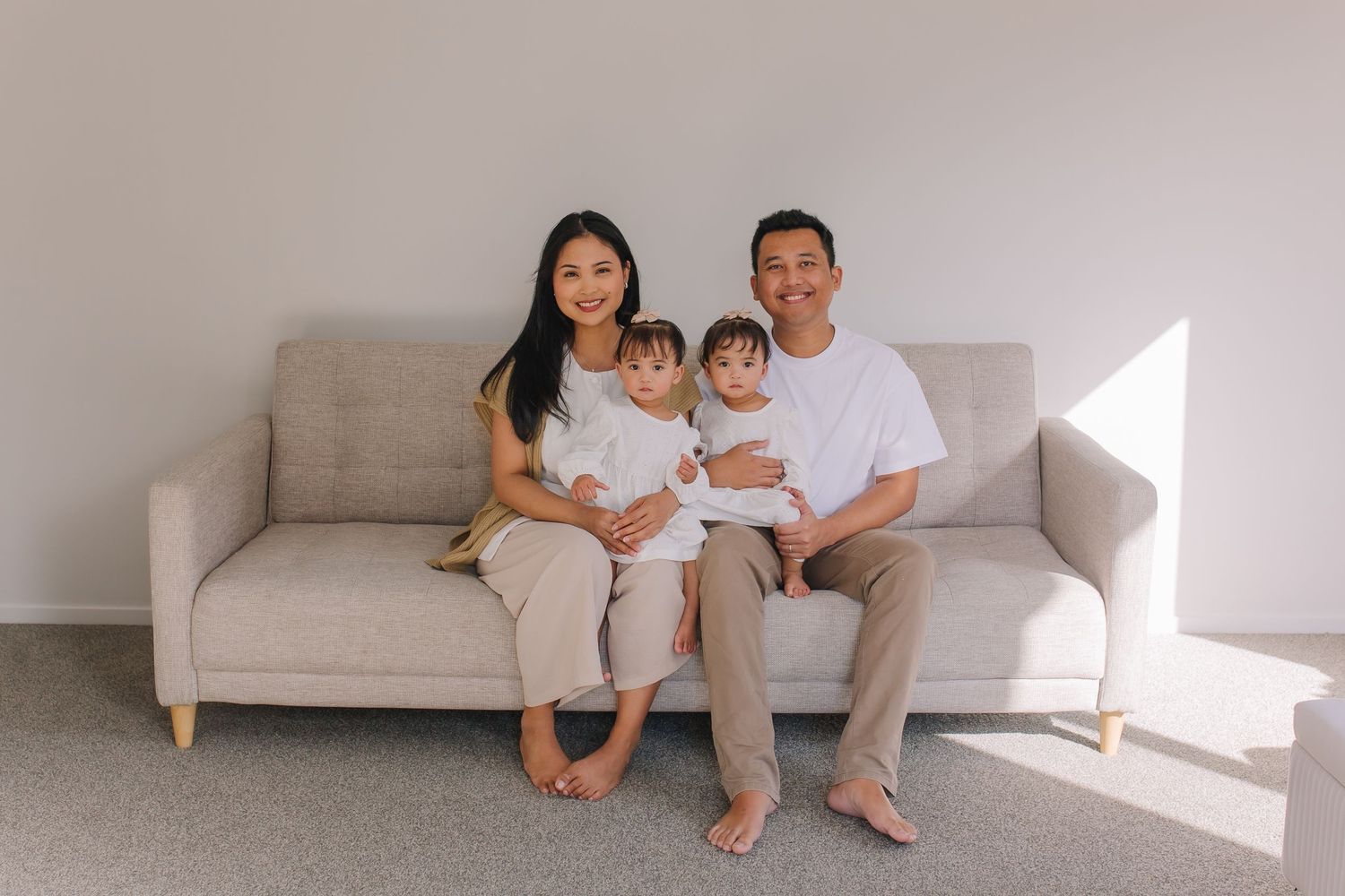 A relaxed family portrait on a light gray couch in a minimalist bright room.