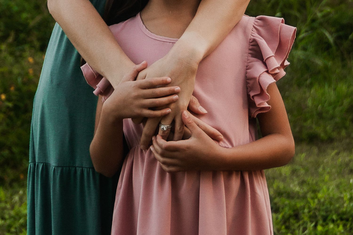 Close-up of hands embracing in pink and green dresses against a natural backdrop.