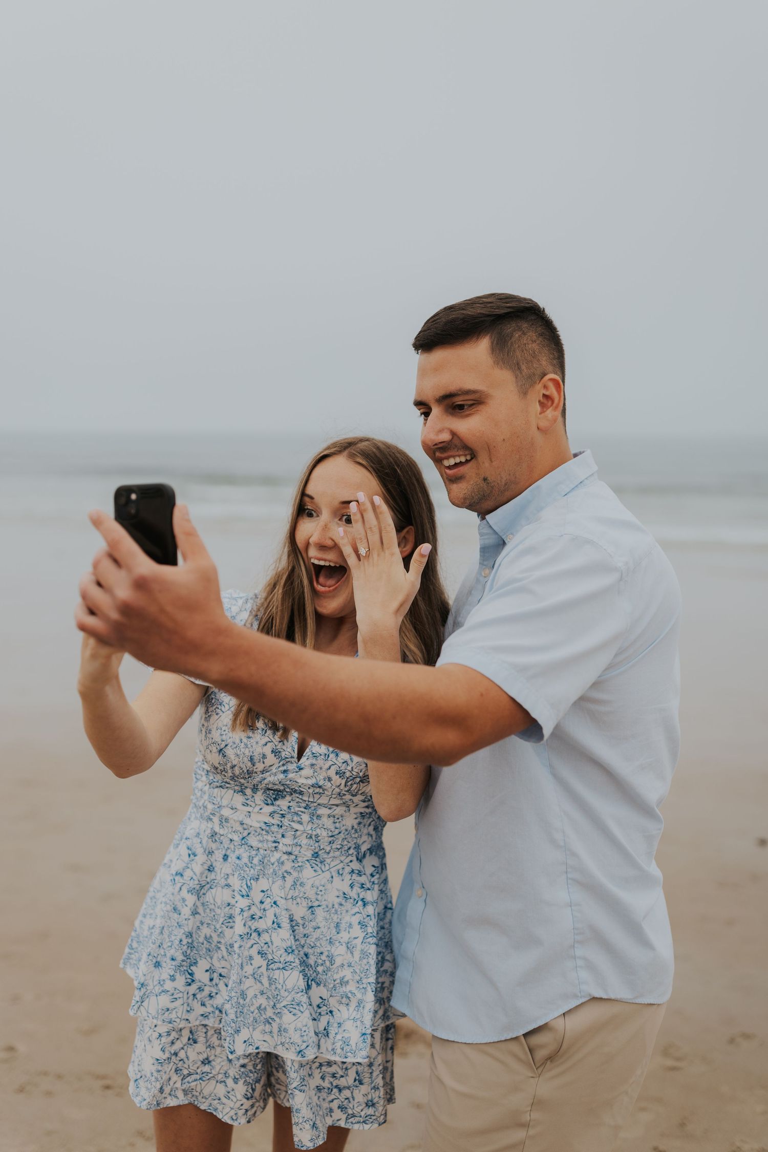 A beachside proposal scene with waves and overcast sky in the background.