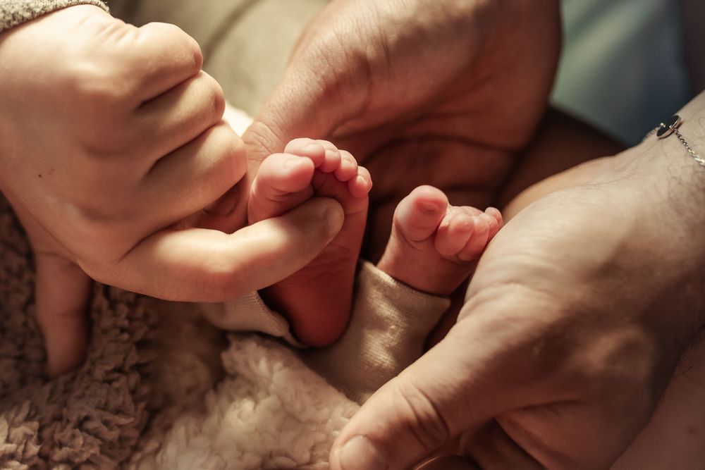 Gentle hands holding tiny newborn feet against textured blanket.