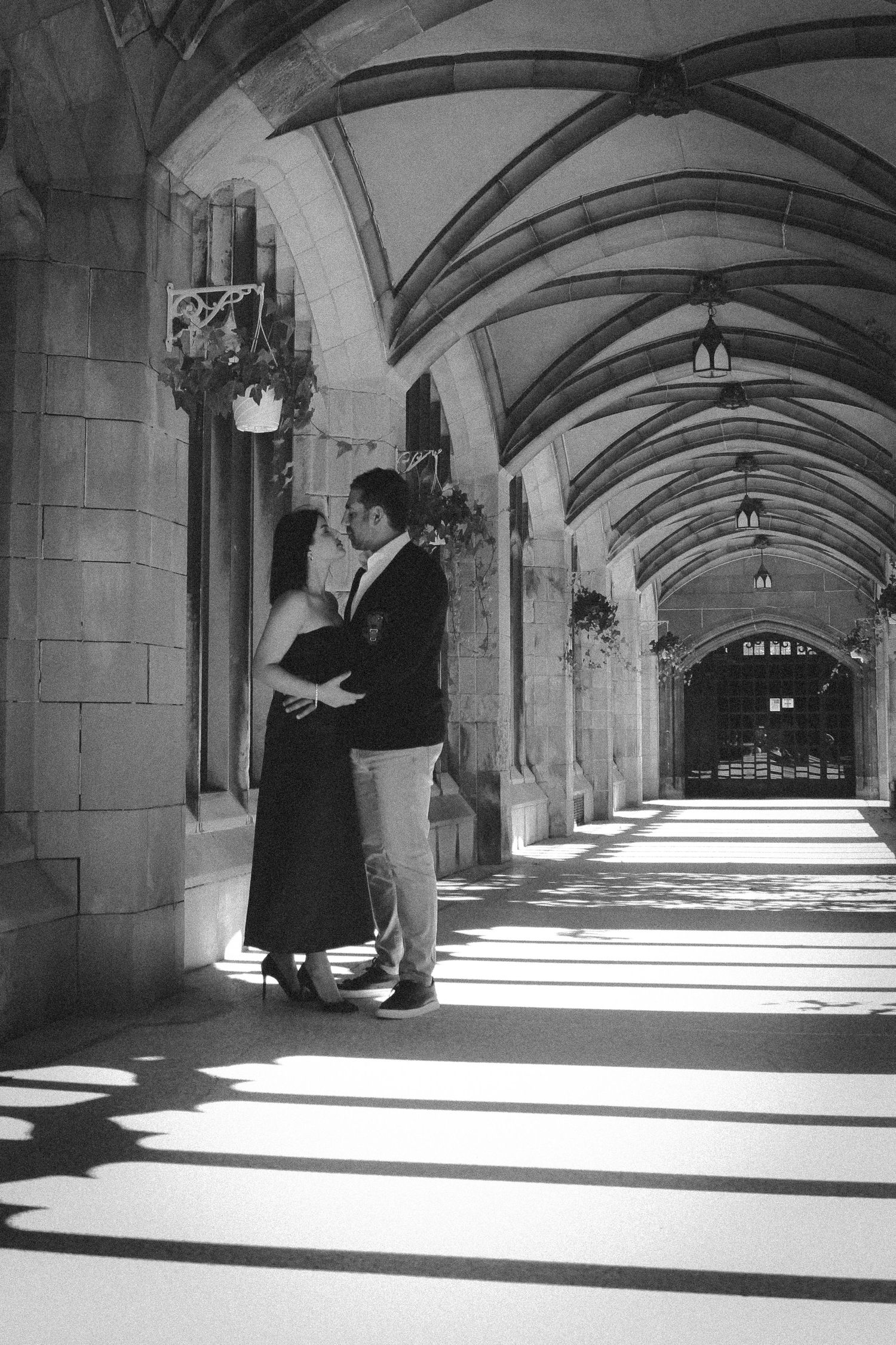 Romantic black and white photo of a couple in an arched stone hallway with dramatic lighting.