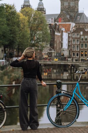 Person posing with blue bicycle along Amsterdam canal with historic architecture in background.