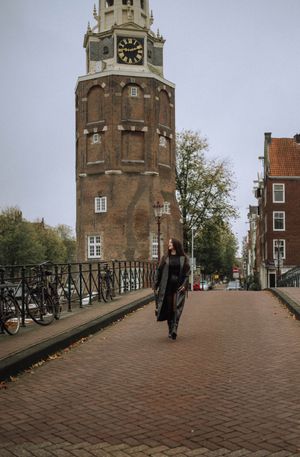 Historic clock tower and brick buildings along cobblestone path in Amsterdam.