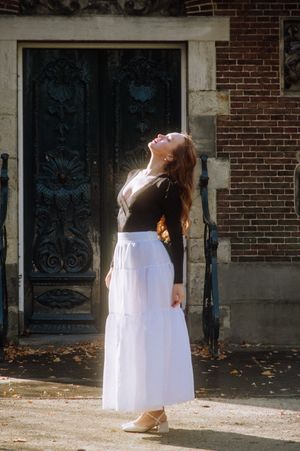 Woman in black top and white skirt poses dramatically by ornate vintage door.