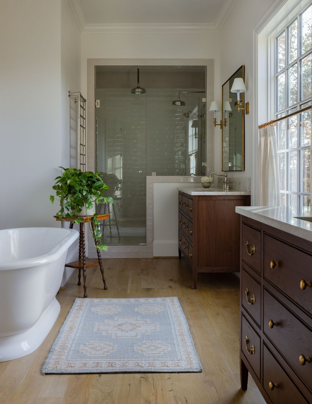 Elegant bathroom with freestanding soaking tub, dark wood vanity, brass fixtures, glass shower, and hardwood floors.