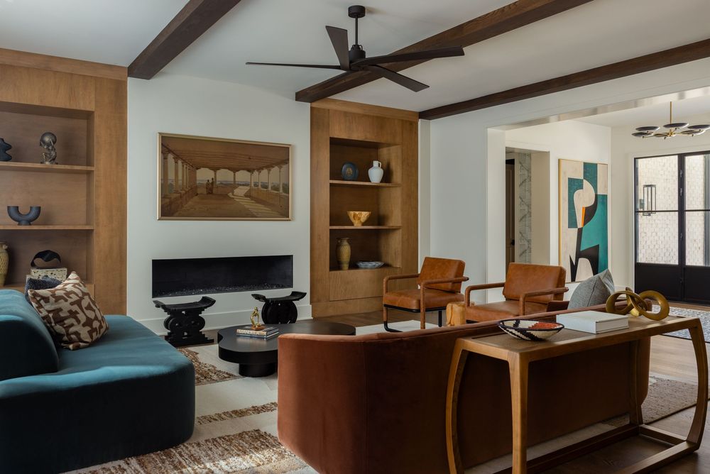 Mid-century modern living room with teal sofa, wood beam ceiling, built-in shelves, ceiling fan, and warm brown leather chairs.
