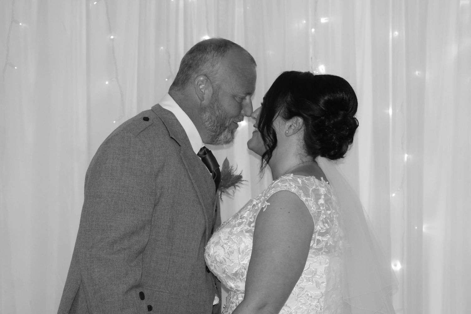 A tender moment between newlyweds captured in black and white with sparkling lights behind them.