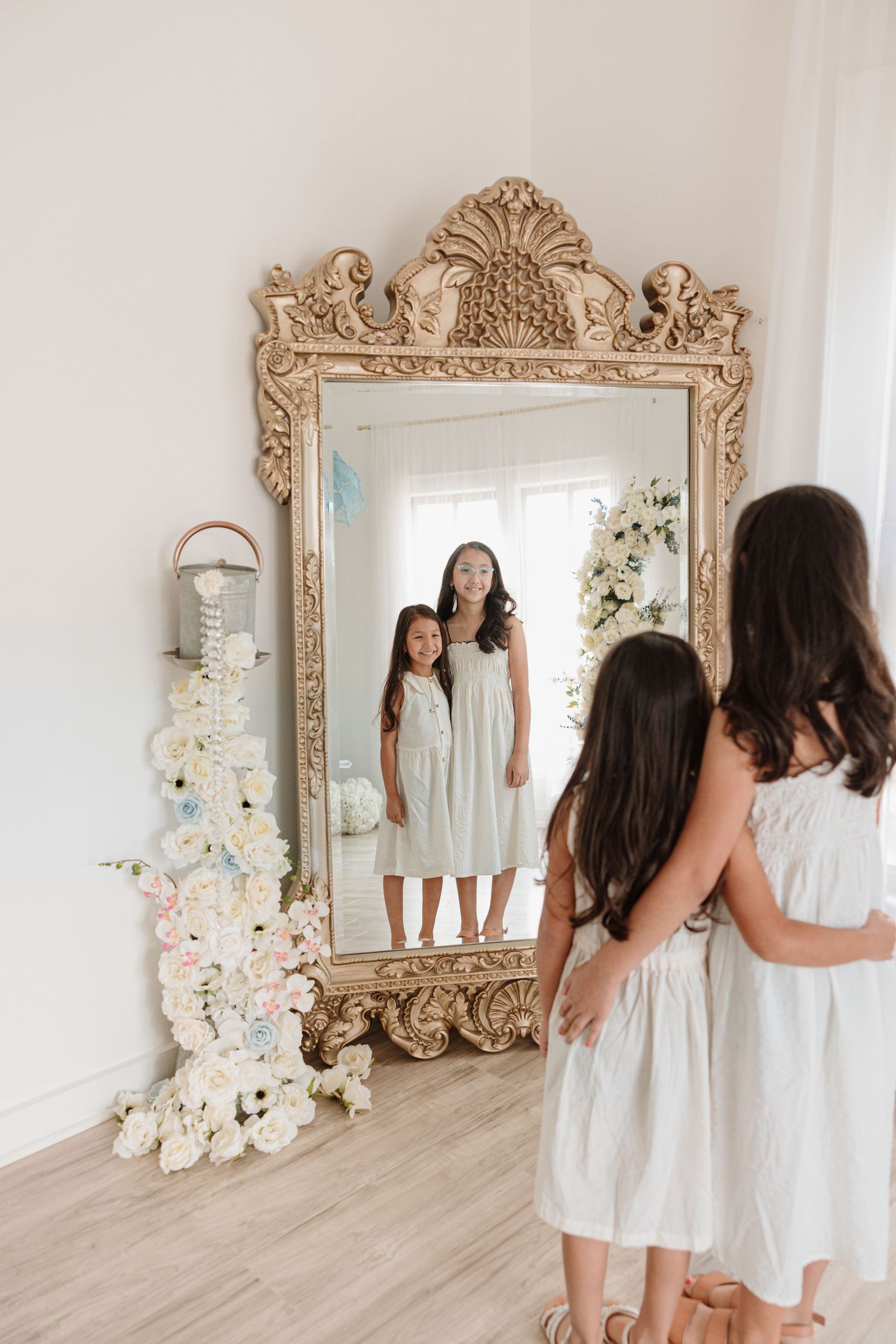 White dresses reflected in ornate gold mirror with floral decorations.
