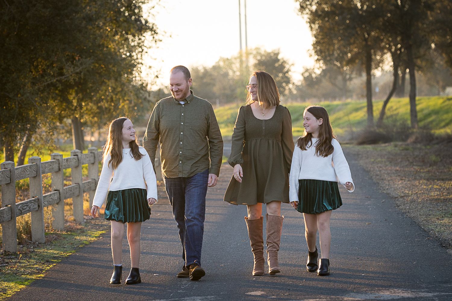 Four people in dark clothing stand together on a green lawn with bushes in the background for outdoor family portraits.