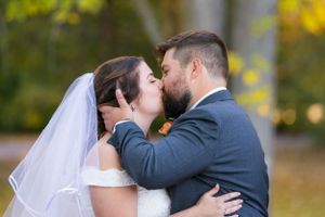 A romantic newlywed couple share an intimate kiss outdoors during an autumn wedding ceremony.