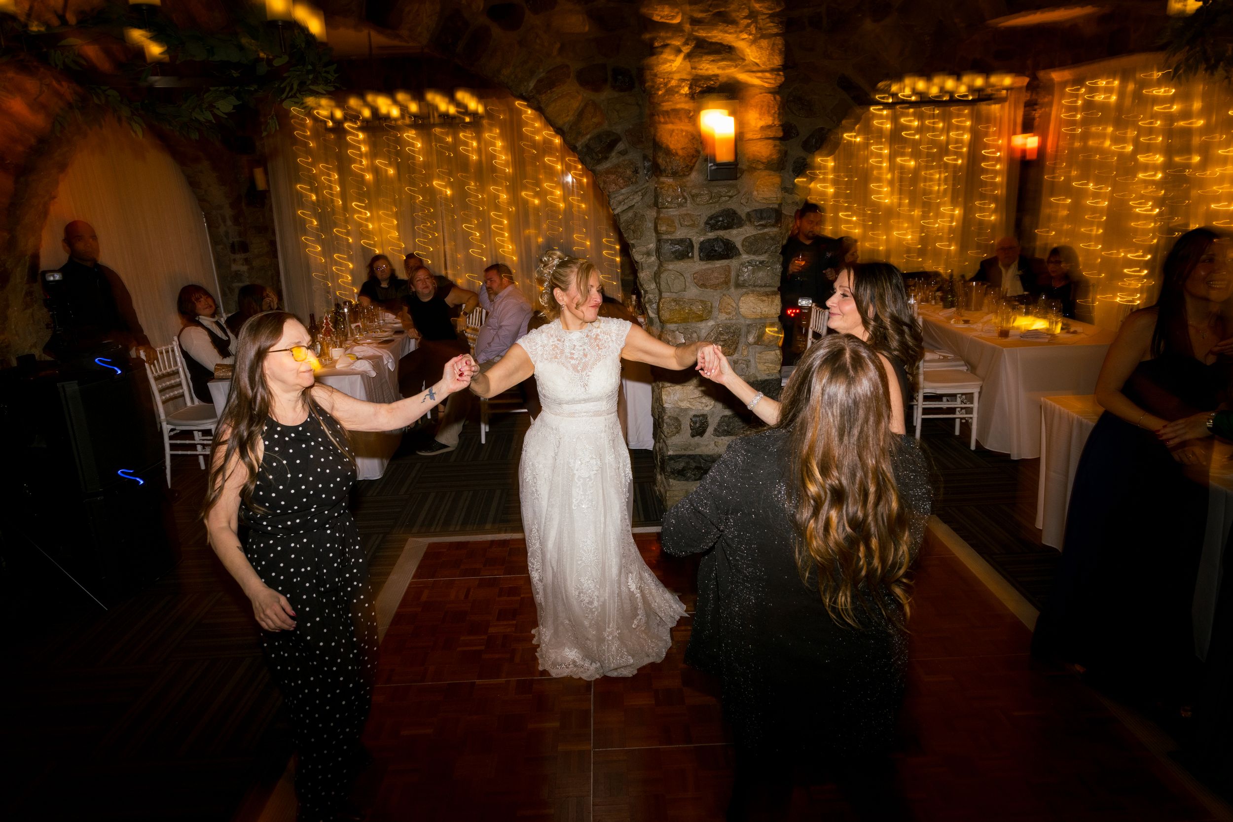 People dance together on a darkened dance floor decorated with string lights at a wedding reception.